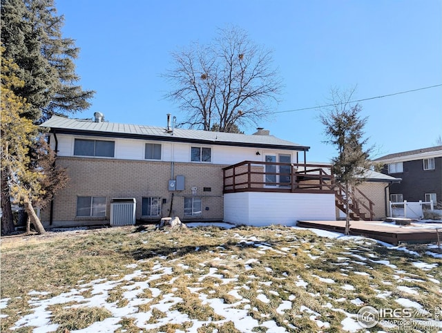 snow covered rear of property with cooling unit, brick siding, a chimney, and a wooden deck