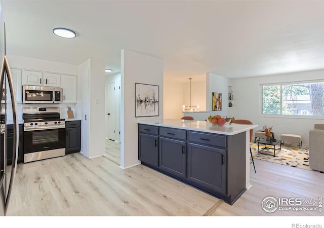 kitchen with decorative light fixtures, a peninsula, stainless steel appliances, light countertops, and white cabinetry