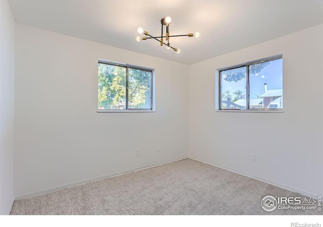 spare room with a notable chandelier, baseboards, a wealth of natural light, and light colored carpet