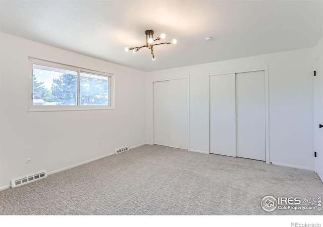 unfurnished bedroom with multiple closets, a chandelier, visible vents, and light carpet