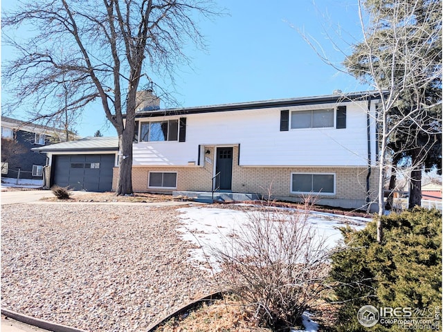 split foyer home with a garage, a chimney, concrete driveway, and brick siding