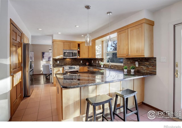 kitchen featuring dark stone countertops, appliances with stainless steel finishes, kitchen peninsula, and light tile patterned floors