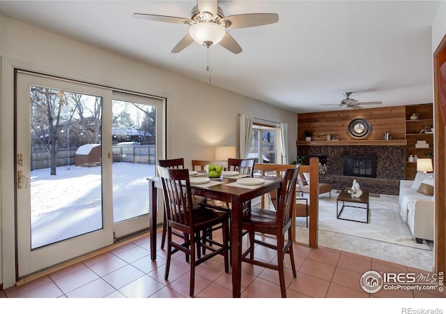 tiled dining room featuring ceiling fan, a fireplace, and wood walls