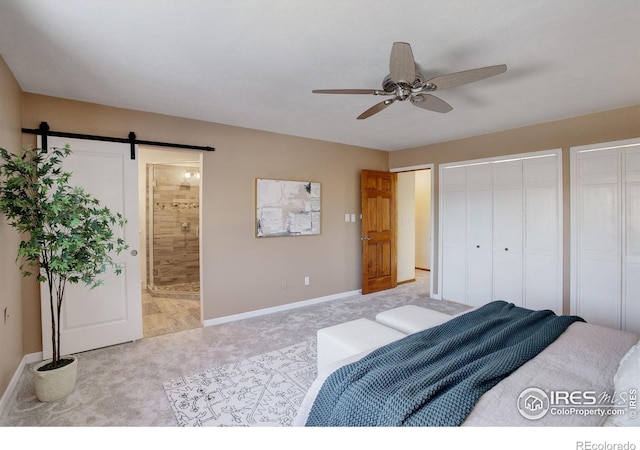 carpeted bedroom with a barn door, connected bathroom, two closets, and ceiling fan