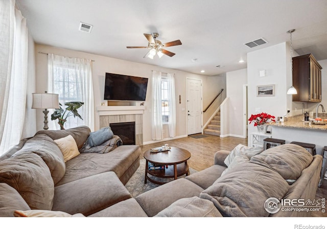 living room with a tile fireplace, ceiling fan, and light hardwood / wood-style flooring