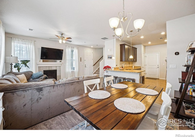 dining space featuring a tiled fireplace, sink, ceiling fan with notable chandelier, and light hardwood / wood-style floors