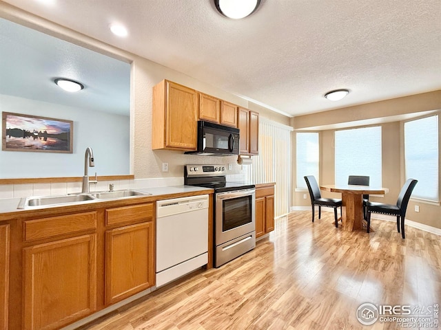 kitchen featuring dishwasher, sink, stainless steel range with electric cooktop, light hardwood / wood-style floors, and a textured ceiling