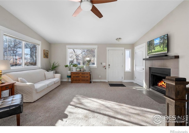 living room with ceiling fan, lofted ceiling, a tile fireplace, and carpet