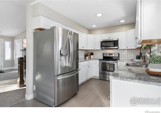 kitchen featuring appliances with stainless steel finishes, tasteful backsplash, sink, white cabinets, and light stone countertops