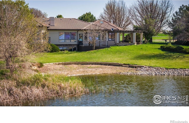 back of property with a water view, a yard, and a pergola