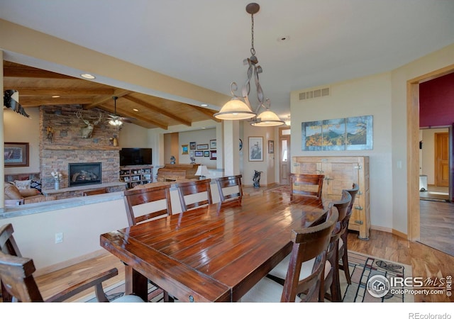 dining area with a stone fireplace, lofted ceiling with beams, and light wood-type flooring