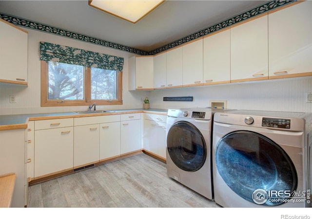 washroom with cabinets, sink, washing machine and clothes dryer, and light hardwood / wood-style flooring