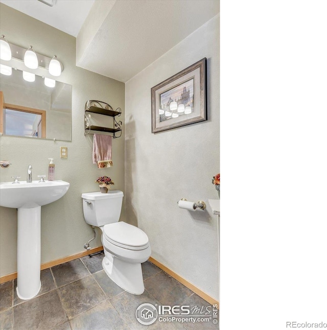 bathroom featuring toilet, baseboards, and a sink