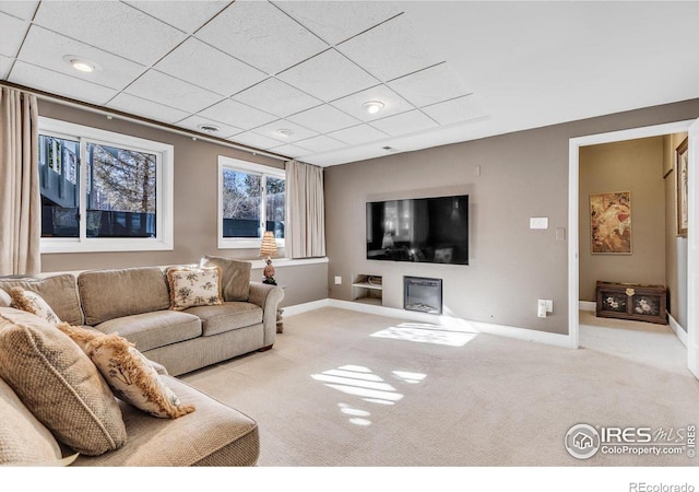 living area with light carpet, a paneled ceiling, and baseboards