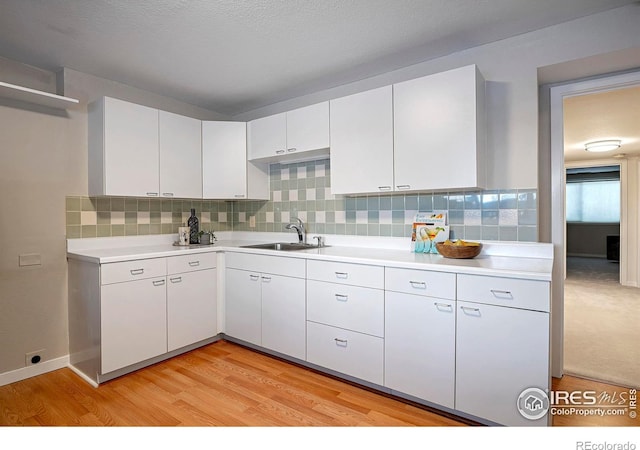 kitchen with tasteful backsplash, sink, light hardwood / wood-style floors, and white cabinets