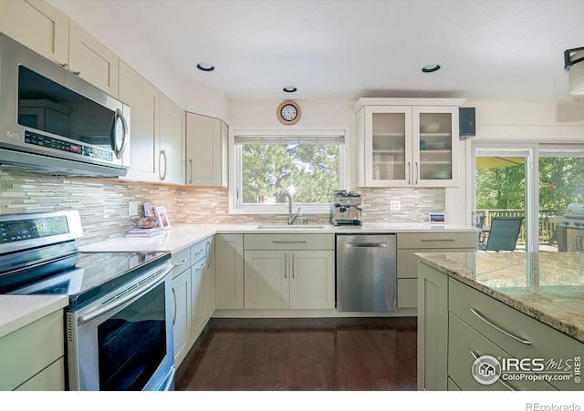 kitchen with sink, dark wood-type flooring, appliances with stainless steel finishes, backsplash, and light stone countertops