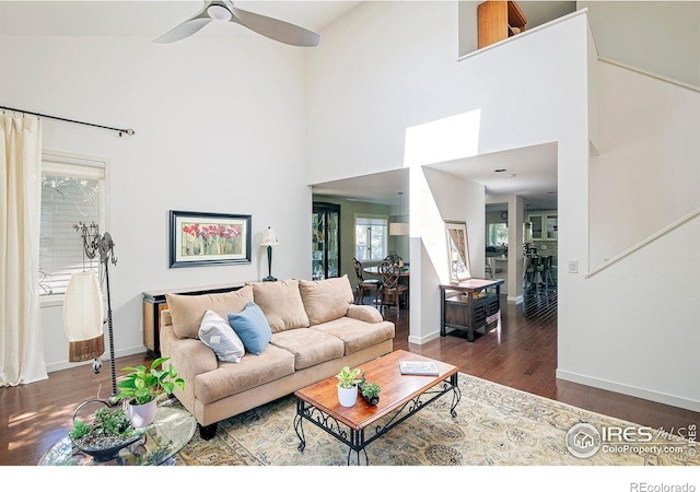 living room featuring dark wood-type flooring, a towering ceiling, and ceiling fan