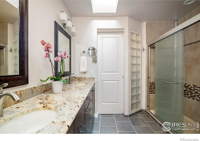 bathroom featuring a skylight, vanity, tile patterned flooring, and a shower with door