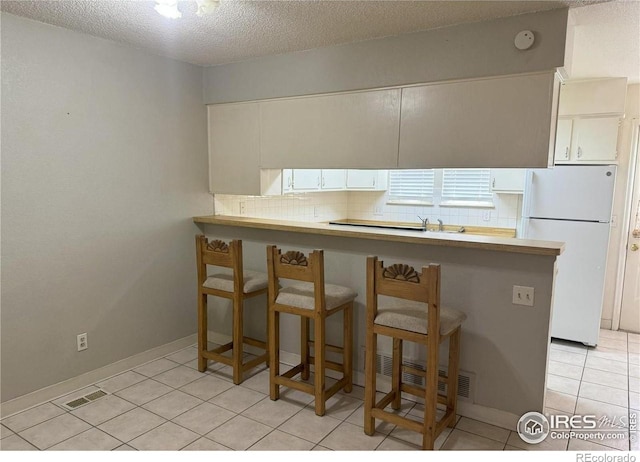 kitchen with a breakfast bar, white refrigerator, kitchen peninsula, white cabinets, and backsplash