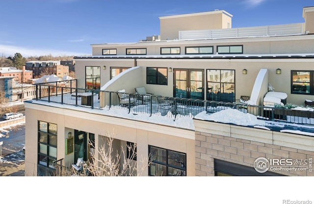 snow covered rear of property featuring stucco siding