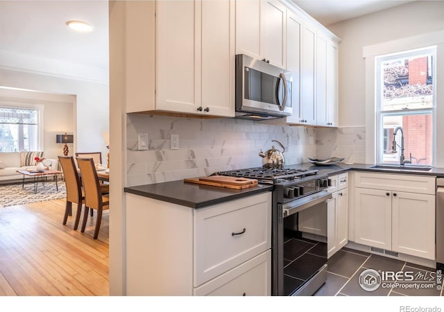 kitchen featuring sink, appliances with stainless steel finishes, white cabinetry, tasteful backsplash, and dark tile patterned flooring