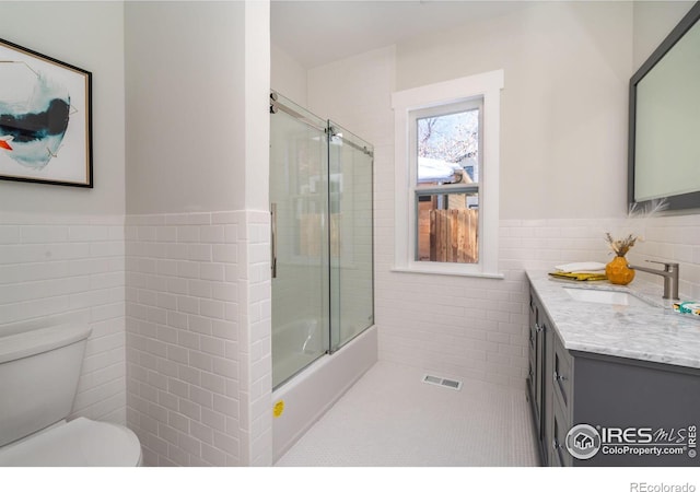 full bathroom featuring tile walls, tile patterned flooring, enclosed tub / shower combo, vanity, and toilet