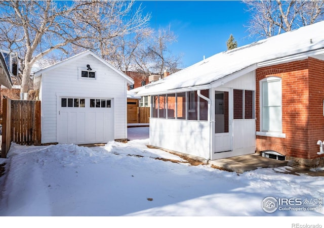 view of snowy exterior featuring a garage, a sunroom, and an outdoor structure