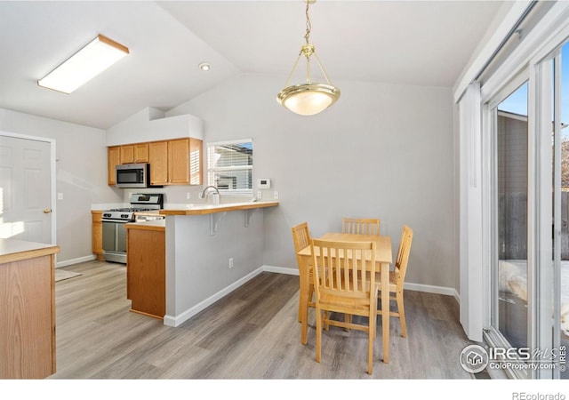 kitchen featuring a breakfast bar area, hanging light fixtures, stainless steel appliances, vaulted ceiling, and kitchen peninsula