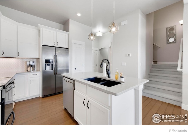 kitchen with stainless steel appliances, a kitchen island with sink, sink, and white cabinets