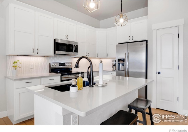 kitchen featuring stainless steel appliances, a center island with sink, white cabinets, and decorative light fixtures