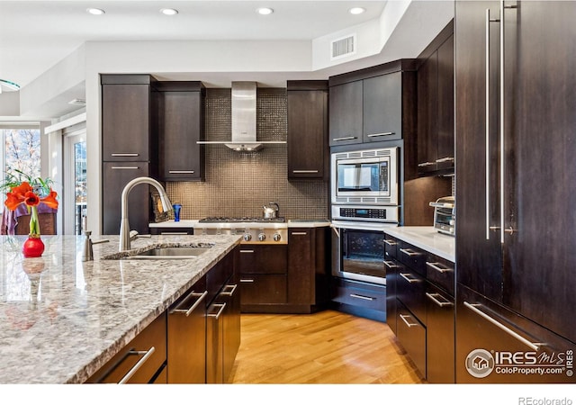 kitchen with sink, appliances with stainless steel finishes, backsplash, light stone countertops, and wall chimney exhaust hood