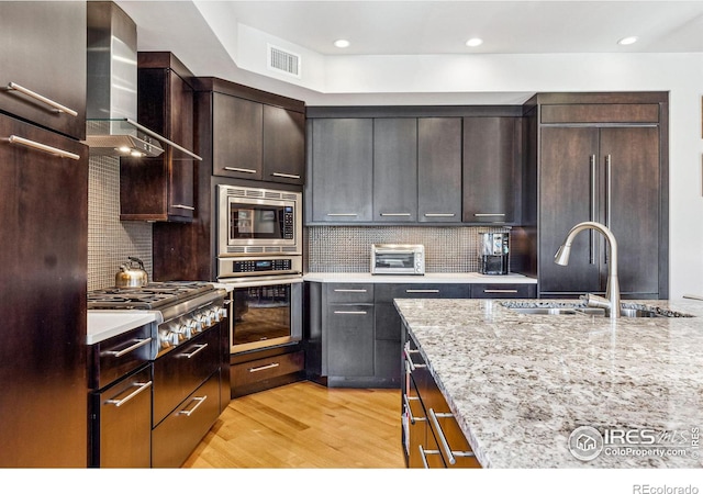 kitchen featuring sink, backsplash, built in appliances, light stone countertops, and wall chimney exhaust hood