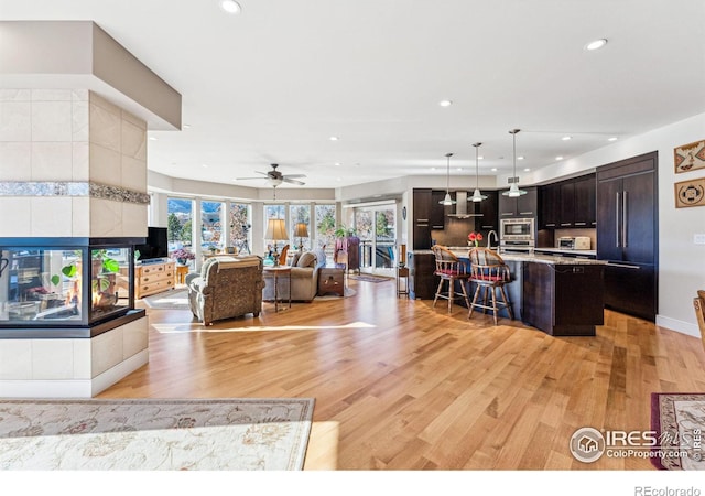 living room featuring sink, a fireplace, light hardwood / wood-style floors, and ceiling fan