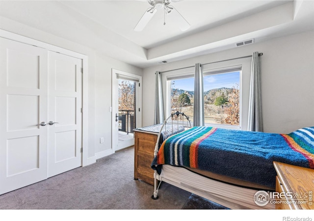 bedroom with access to exterior, a tray ceiling, carpet floors, and ceiling fan