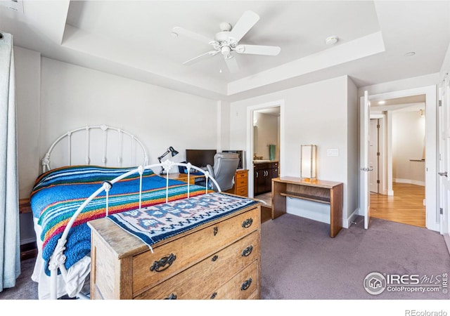 carpeted bedroom featuring ceiling fan, ensuite bath, and a tray ceiling