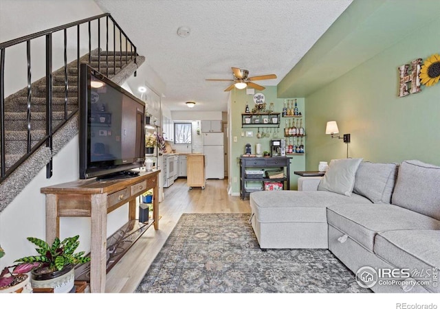 living room with ceiling fan, a textured ceiling, and light hardwood / wood-style floors