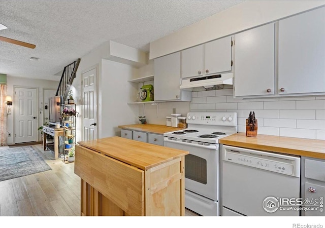 kitchen with butcher block counters, decorative backsplash, white appliances, a textured ceiling, and light hardwood / wood-style flooring