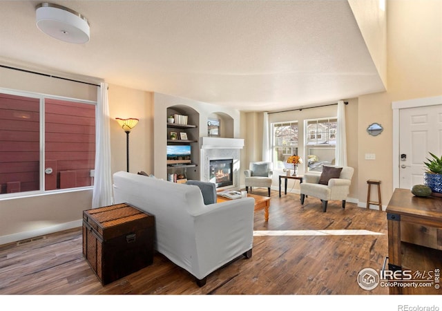 living area with a glass covered fireplace, wood finished floors, visible vents, and baseboards