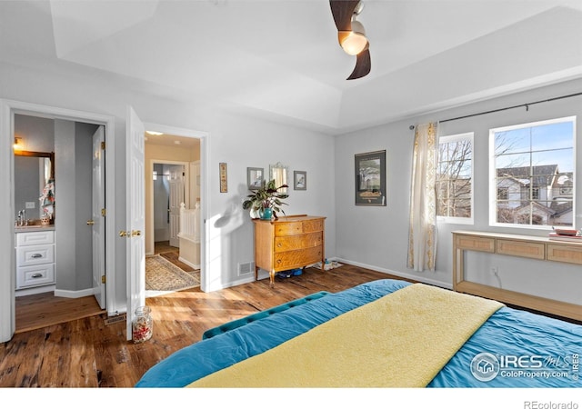 bedroom with connected bathroom, ceiling fan, baseboards, a tray ceiling, and wood finished floors