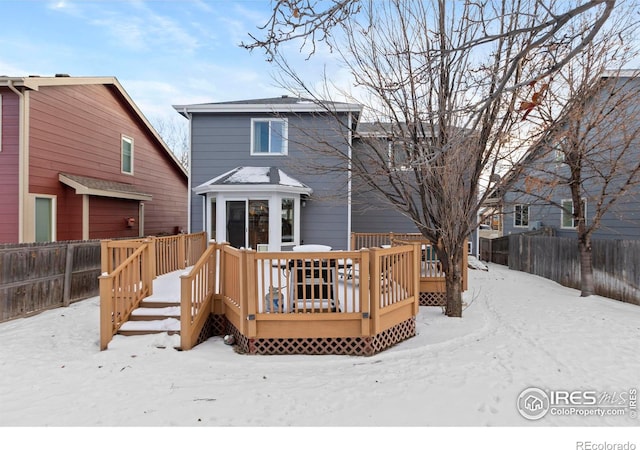 snow covered back of property featuring a wooden deck and fence