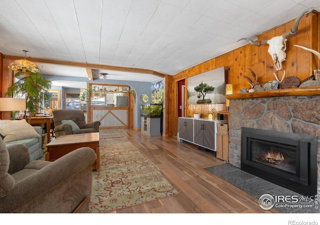 living room featuring a stone fireplace, wood finished floors, and wood walls