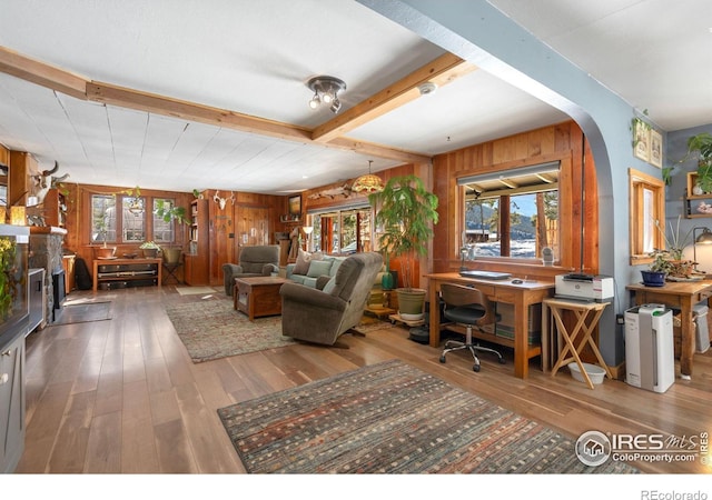 living area featuring beamed ceiling, plenty of natural light, wood finished floors, and wood walls