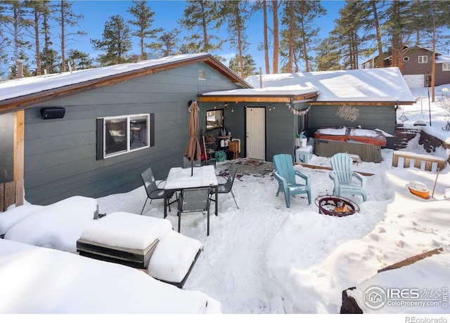 snow covered rear of property with outdoor dining space, a patio, and a hot tub