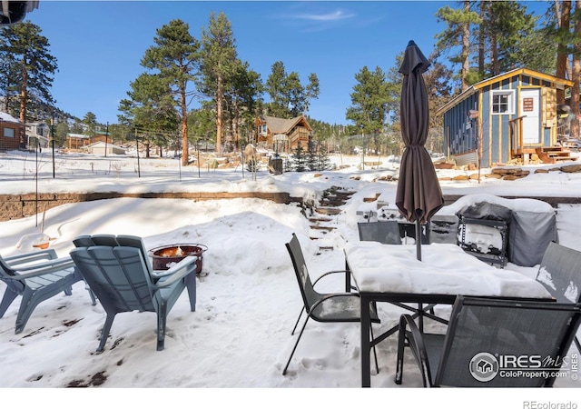 snow covered patio featuring an outbuilding, outdoor dining area, and an outdoor fire pit