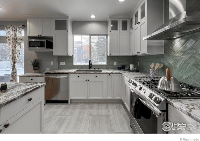 kitchen featuring appliances with stainless steel finishes, sink, backsplash, light stone countertops, and wall chimney range hood