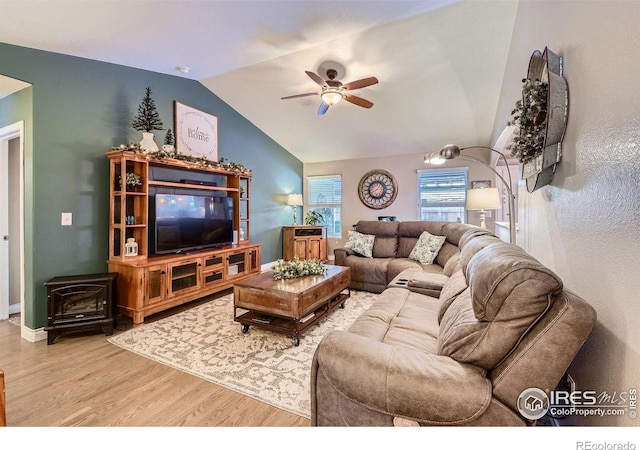 living room with hardwood / wood-style flooring, ceiling fan, vaulted ceiling, and a wood stove