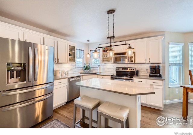 kitchen with stainless steel appliances, a kitchen island, pendant lighting, and white cabinets