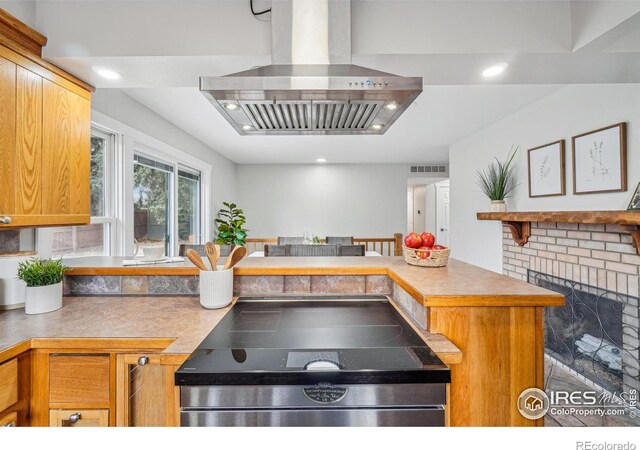 kitchen with island exhaust hood, a fireplace, and kitchen peninsula