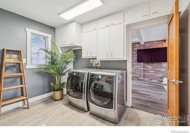 laundry area with cabinets, brick wall, washing machine and clothes dryer, and light hardwood / wood-style floors