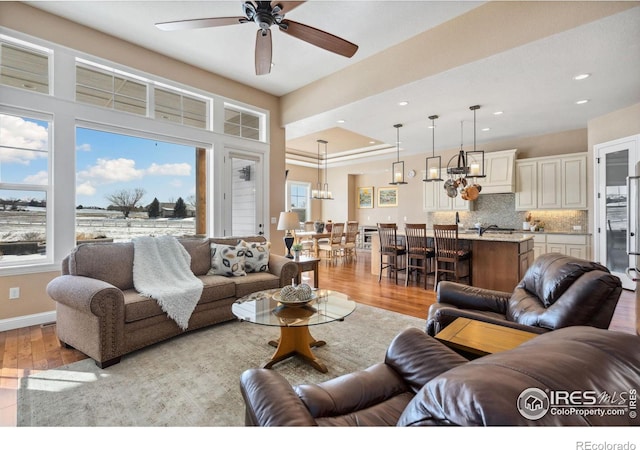 living room featuring ceiling fan with notable chandelier and light wood-type flooring